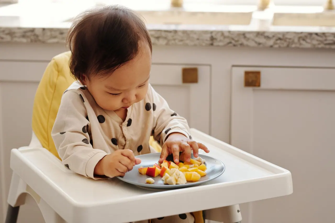 Niño sentado en una trona explorando la comida con las manos